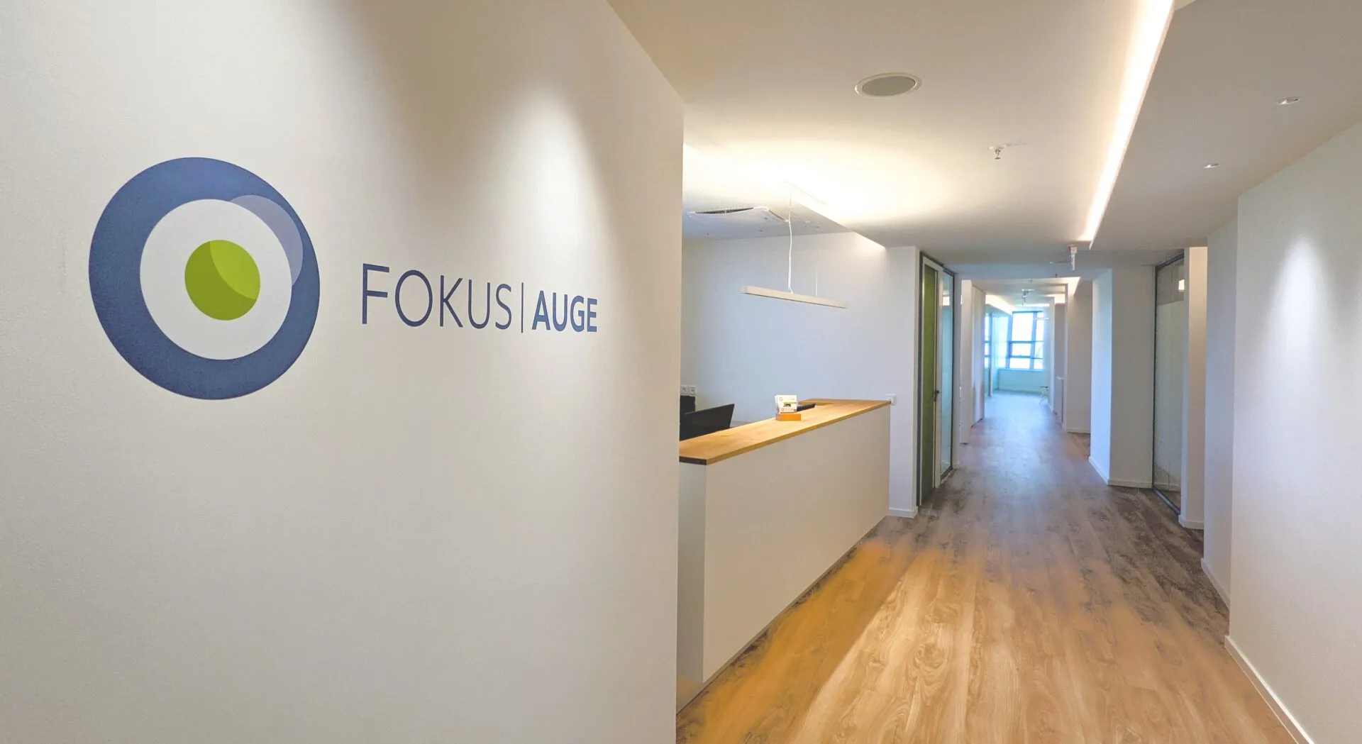 Wandlogo FOKUS AUGE neben dem Empfangstresen mit Blick in den Flur
