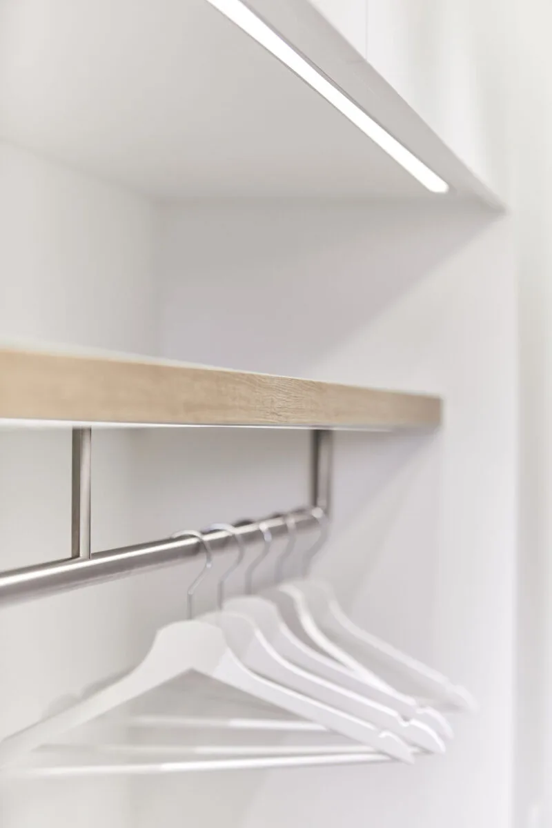 Garderobe mit weißen Kleiderbügeln an einer Stange unter einem Holzboard