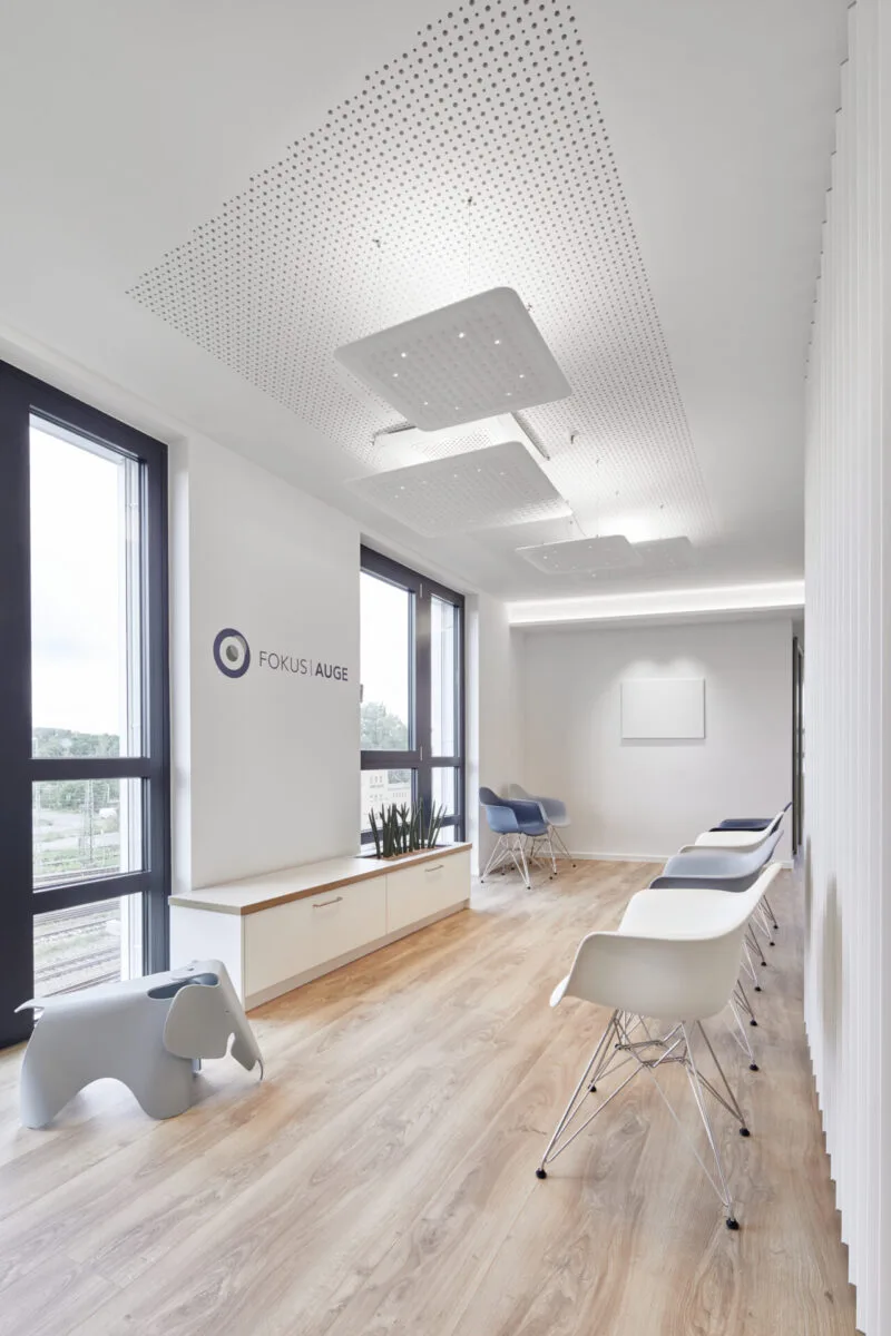 Heller Wartebereich mit Fensterfront, Stühlen im Schalenstil, einer Sitzbank und Wandlogo FOKUS AUGE