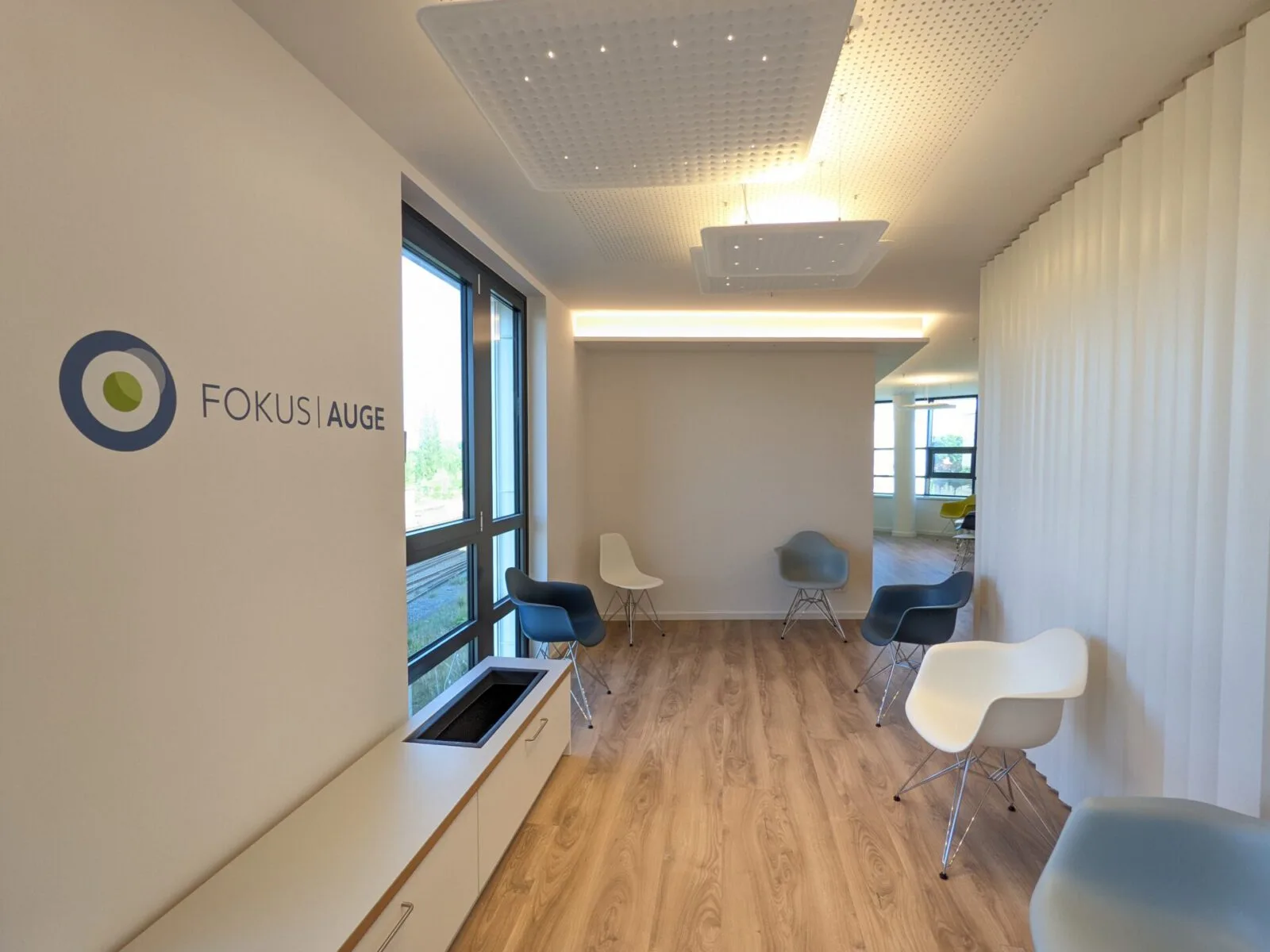 Wartebereich mit Wandlogo FOKUS AUGE, Fensterfront und Schalenstühlen
